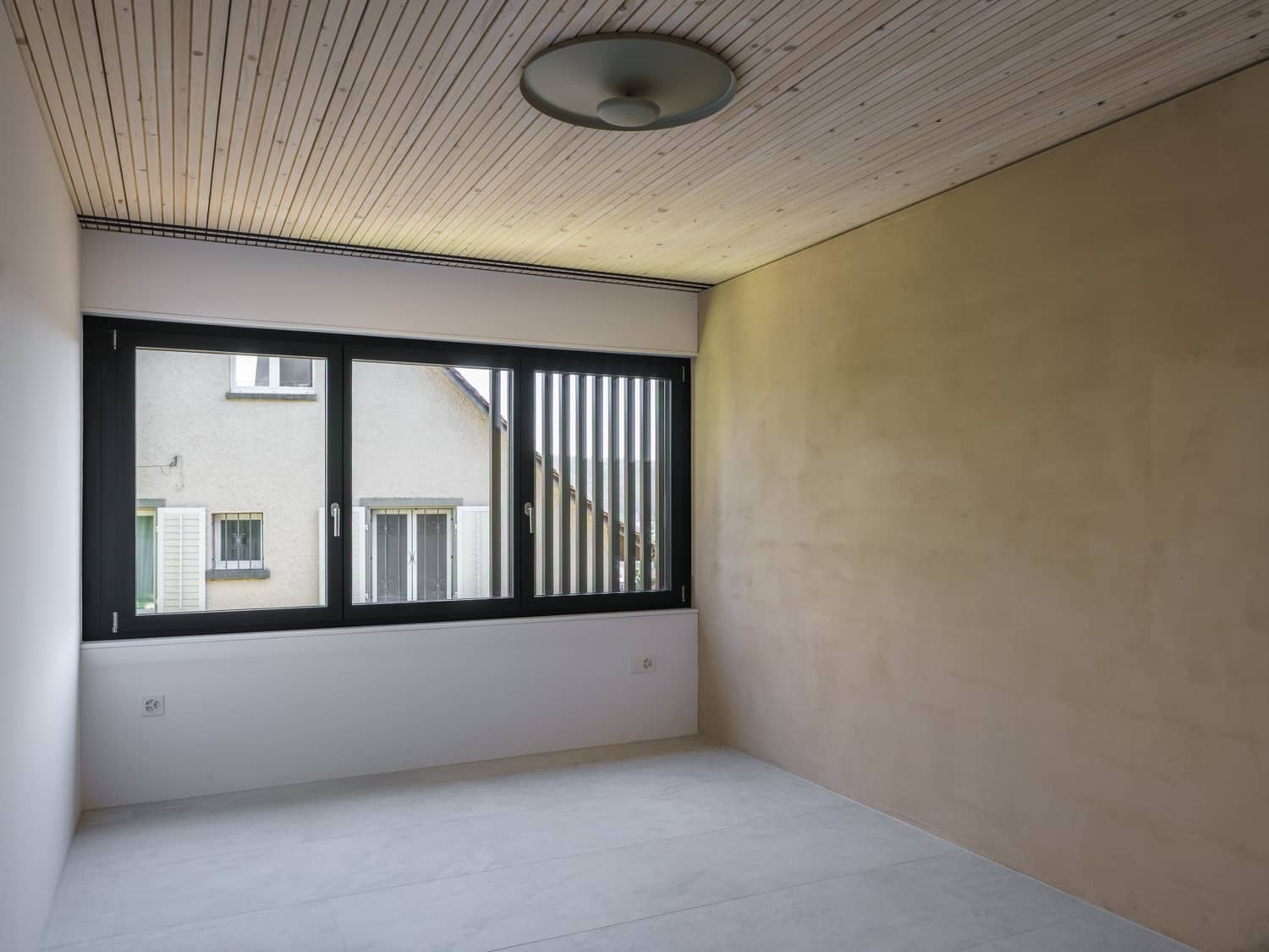 Ein leerer Raum mit grossem Fenster, der in der Nacht durch eine stilvole Deckenlampe beleuchtet werden kann